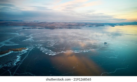 Aerial photography of Lake Baikal in winter at dawn. Beautiful view of the frozen lake. Clouds are reflected on the transparent ice.