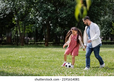 公園の牧草地でお父さんとサッカーをしている陽気なアジアの子供