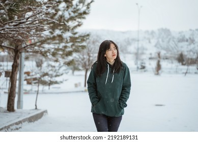 mujer asiática con capucha verde caminando sola en un lugar nevado mirando hacia otro lado