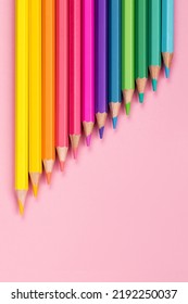 Houten pastelkleurige regenboogkleuren potloden close-up op roze papieren achtergrond, verticale opstelling van het bovenaanzicht. Het concept van terug naar school, een voorbeeld screensaver voor een tekenstudio voor kinderen.