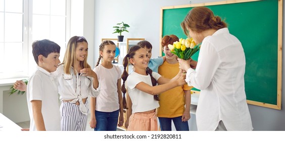 Leuke schoolkinderen met bloemen voor hun beste vrouwelijke leraar op school ter ere van vakantie. Preteen klasgenoten in de klas geven leraar boeket tulpen. Dag van de leraar concept. Webbanner.