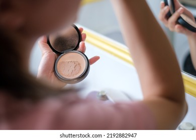 Cropped image side view asian young woman doing make up with powder standing in bathroom near mirror. Routine bodycare.