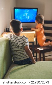 Rear view of a boy sitting on the sofa watching a cartoon on the computer with his sister. Modern technology. Children smart technology gadget usage concept