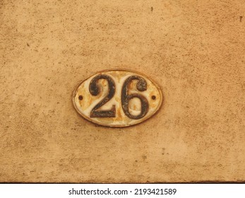 House number (address) twenty six (26) sign, black numbered white plate (closeup) against cream and off white wall of old building background. Grunge, texture, wallpaper   