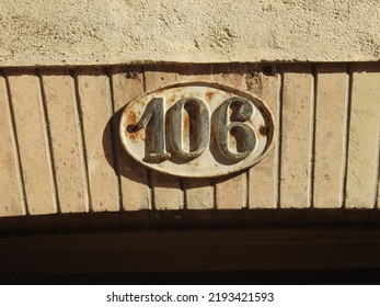 House number (address) one hundred and six (106) sign, black numbered plate (closeup) against bricks and off white wall of old building background. Grunge, texture, wallpaper