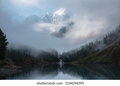 雲の中に雪の城がある静かな風景。マウンテン クリークは、森の丘から氷河湖に流れ込みます。霧のクリアランスの雪山。穏やかな高山湖に映る小さな川と針葉樹。