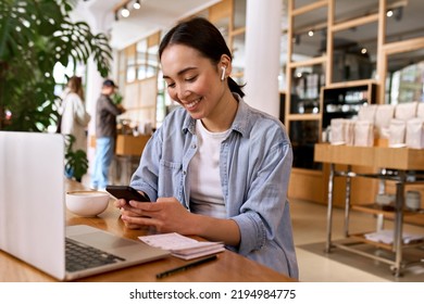 Młoda, uśmiechnięta azjatycka studentka korzysta ze smartfona do e-learningu, ma założone słuchawki douszne, ogląda szkolenie online w aplikacji mobilnej, uczy się i prowadzi hybrydową rozmowę wideo na telefonie komórkowym.