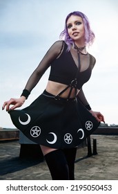 Portrait of pretty smiling gothic girl on the roof. Pastel goth with violet (purple) hair in black clothes