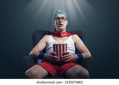 Funny superhero watching movies and eating popcorn, he is staring at the screen with mouth open