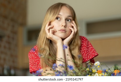Romantic girl in a red dress with a bouquet of wild flowers looks into the distance