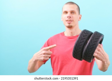 男は 2 つの小さなスクーター タイヤを保持し、青い背景に指を指しています。車輪。ゴム。黒。交通手段。車両。タイヤ。部。修理。良い。優秀な。修理。修理済み