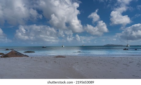 Fußspuren sind am Sandstrand sichtbar. Felsbrocken in der Nähe des Wassers. Weiße Yachten im türkisfarbenen Ozean. Malerische Kumuluswolken am blauen Himmel. Seychellen. Insel Praslin. Anse Lazio-Strand