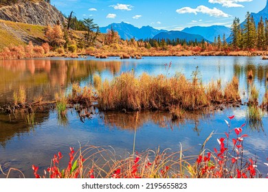 Indian summer in the Rocky Mountains. Red and yellow foliage of the autumn forest on the shores of the lake. The smooth cold water of Lake Vermillon reflects the snow-white clouds