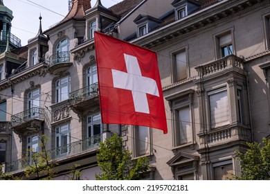 Zoomopname van een felrode Zwitserse vlag met een wit kruis dat zachtjes waait in de lichte bries tegen een onscherpe achtergrond.