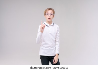 ちょうどアイデアを持っている眼鏡をかけた肖像画のハンサムな白人少年は、白い学校の t シャツで指を指しています。灰色の背景に分離