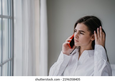 Tânără hispanic brunetă frustrată care vorbește la telefon cu soțul, în necazuri. Fată destul de caucaziană acasă folosind telefonul mobil privind fără speranță la fereastră. Gospodina suparata. Machetă fată tristă.