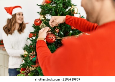 Young hispanic couple decorating christmas tree at home.