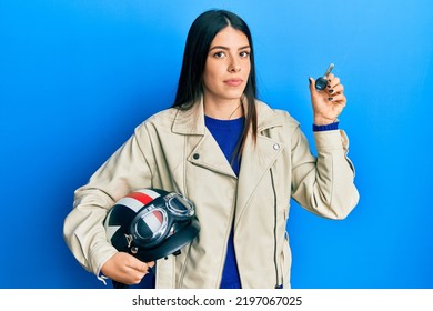 Người phụ nữ trẻ gốc Tây Ban Nha cầm mũ bảo hiểm và chìa khóa xe máy thư giãn với vẻ mặt nghiêm túc. đơn giản và tự nhiên khi nhìn vào máy ảnh.