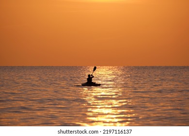 Dark silhouette of lonely fisherman rowing on his boat on sea water at sunset