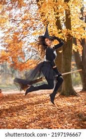 Woman in witch costume standing in autumn forest on Halloween