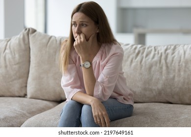 自宅のソファに座り、目をそらし、健康上の問題、危機、喪失、悪いニュースを考え、顔に触れ、ストレスを感じ、イライラする不幸な落ち込んだきれいな女性。負の感情