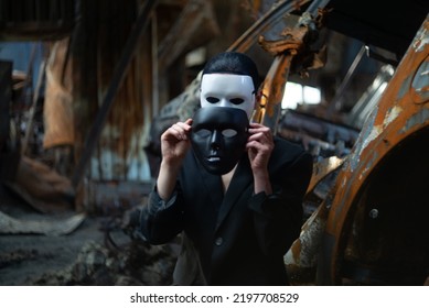 Een meisje in een zwart pak en een wit masker zit naast een uitgebrande auto, nadat een Russische legergranaat het huis heeft geraakt.