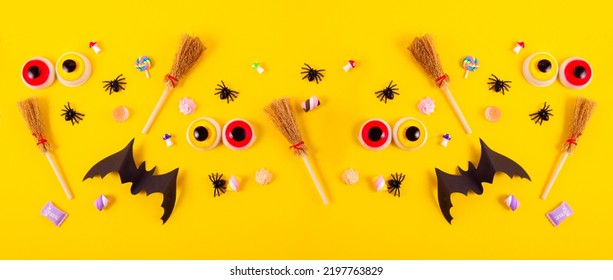 Halloween frame with pumpkins, spiders, and paper cut-out bats against a bright yellow background. Big eyes and witches brooms on a Top view Halloween concept.