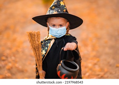 Portrait of cute Little Girl in costume of hat in the park. Happy Halloween during coronavirus covid-19 pandemic quarantine concept. Kid wearing medical mask