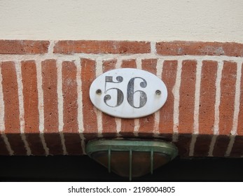 House number (address) fifty six (56) sign, black numbered white plate (closeup) against red (orange) bricks wall of old building background. Grunge, texture, wallpaper