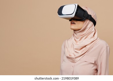 Jonge Arabische Aziatische moslimvrouw die ze draagt ​​abaya hijab roze kleding horloge in vr headset pc gadget geïsoleerd op effen pastel licht beige achtergrond Mensen vae Midden-Oosten islam religieus concept