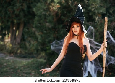 Halloween Beautiful young Witch girl in witches hat on spooky dark magic forest background. with carved Pumpkin. redhead girl with big eyes magical sight