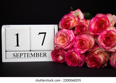 September 17 wooden calendar, white on a black background, pink roses lie nearby.Postcard with copy space. The concept of a holiday, congratulation, invitation, party, announcement, vacation,promotion
