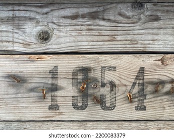 Op een verweerd houten bord staat in zwarte verf het nummer 1954