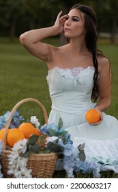 青いドレスを着てオレンジを持った若い美しい白人モデルの夏のポートレート。彼女はオレンジと花でいっぱいのかごを横に持っています。彼女は野原に座っています。