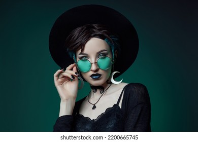 Joven bruja de Halloween con un sombrero redondo y gafas redondas verdes sobre un fondo verde oscuro. Cabello teñido, lápiz labial oscuro, aretes de luna creciente.