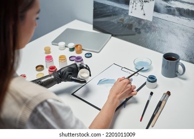 Cận cảnh cô gái trẻ với bức tranh vẽ cánh tay giả trên giấy bằng sơn trên bàn