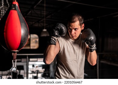 Bokser in verdedigingspositie die op het punt staat een klap uit te delen aan een bokszak. Kortharige blanke man met bokshandschoenen in een sportschool.