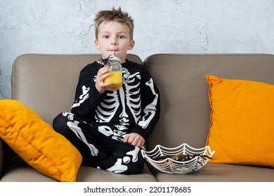 Happy crazy halloween boy having fun at home drinking  scary drink and looking at camera wearing Halloween costume skeleton on home background.