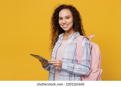 Nhìn từ phía trẻ mỉm cười vui vẻ vui vẻ sinh viên cô gái tuổi teen da đen mát mẻ, cô ấy mặc quần áo bình thường túi ba lô máy tính bảng máy tính bị cô lập trên nền màu vàng trơn. Trung học đại học đại học khái niệm