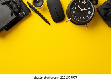 ブラックフライデーセールのコンセプト。空のスペースで分離された黄色の背景に黒のギフト ボックスの紙袋目覚まし時計ペン キャンドル コンピューター マウスとキーボードの上から見た写真