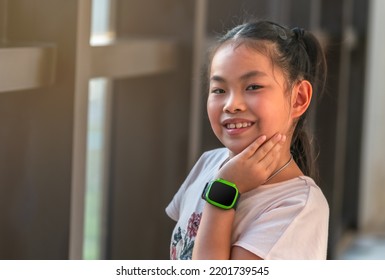 Portret van een schattig Aziatisch kindmeisje, dat naast het glazen raam staat, lacht en naar de camera kijkt, schattig poseert met één hand die de wang aanraakt, een digitaal horloge draagt, een lege weergave van het horloge.