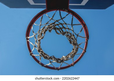 Basketballkorb mit Gitter auf blauem Himmelshintergrund mit Kopierraumhintergrund. Ansicht von unten. Sportmannschaftsspiel Basketball, Streetball.