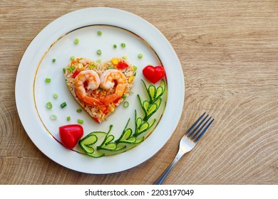Heart shaped shrimp fried rice served with heart shaped cucumbers and tomatoes on plate with wooden background.Creative art food idea for Valentine or Mother's day.Top view.Copy space