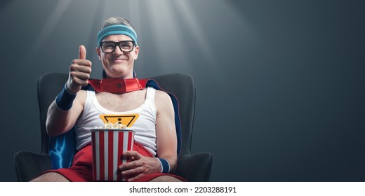 Funny happy superhero watching movies and eating popcorn, he likes the movie and gives a thumbs up