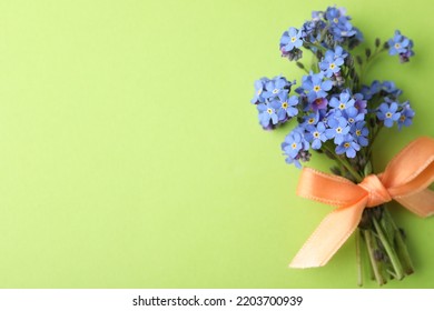 明るい緑の背景、上面にリボンで結ばれた美しい青いワスレナグサの花。テキスト用のスペース