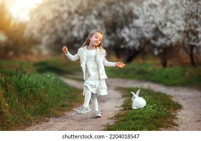 En lille pige danser på vejen ved solnedgang. Glad barndom. En pige med en kanin leger på engen.