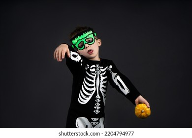  Little fun Happy halloween zombi boy holding pumpkin  looking at camera and open mouth with shocked wearing Halloween skeleton on dark background with copy space for text