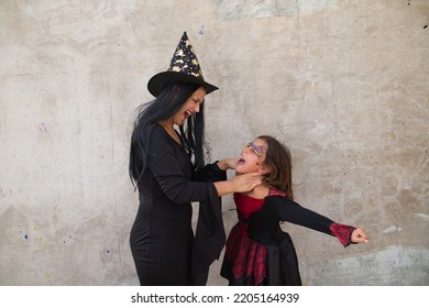 Feliz Halloween. Una joven y una chica vestidas de brujas de fondo gris juegan con gestos aterradores y estranguladores mientras se divierten. Truco o trato.
