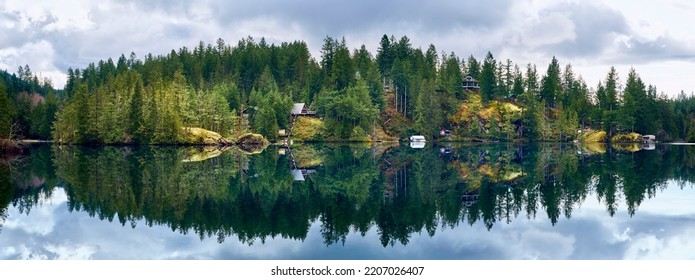 Las casas en las rocas entre el bosque de coníferas se reflejan en el agua cristalina del lago Ruby salvaje en un clima tranquilo. Paisaje forestal en Dan Bosch Park, Sunshine Coast Hwy, BC, Canadá