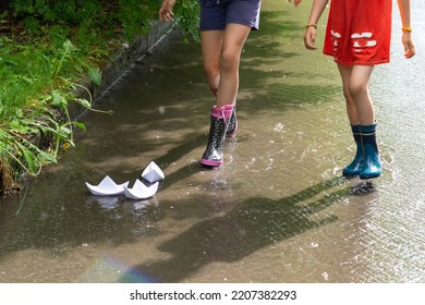 Dua anak bermain dengan perahu kertas di aliran air setelah hujan di trotoar kota